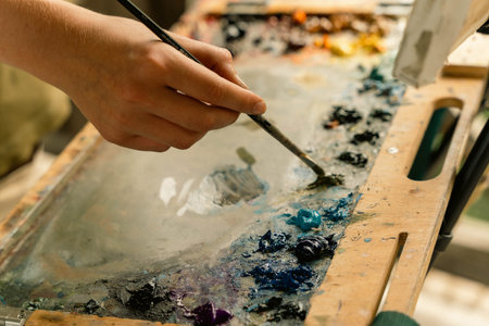 A hand is carefully mixing colors on a wooden paletteの写真素材