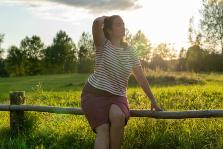 A woman relaxes on a fence while soaking in the sunsetの写真素材