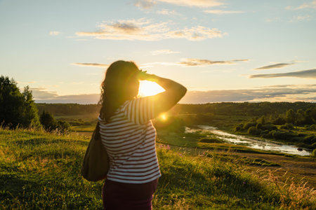 A woman stands admiring a vibrant sunset over a riverの写真素材