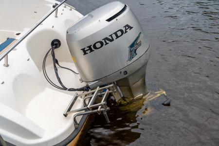 Pskov Region, Russia , July 17, 2024 - Honda outboard motor attached to a boat near a tranquil lakeshoreのeditorial素材