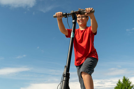 A young boy enjoys riding his scooter under a bright blue sky.