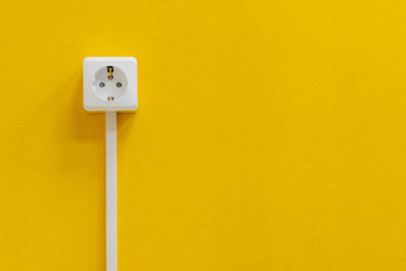 A white electrical socket is affixed to a bright yellow wall. copy spaceの写真素材
