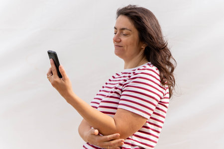 Middle-Aged Woman with Long Hair Using Smartphone on Light Backgroundの写真素材