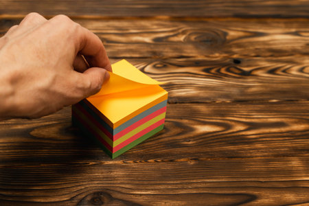 hand tears off a colored sticker to record reminders on Wooden Table. self-adhesive stickers for notesの写真素材