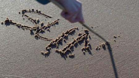 Woman is drawing the words summer time on the sand with a stickの写真素材