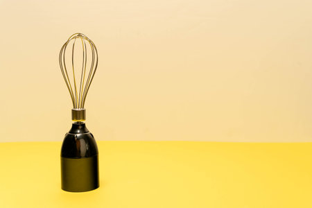 A modern whisk is positioned upright on a yellow surfaceの写真素材