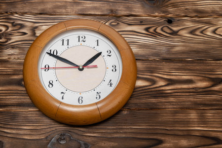 A round clock shows the time against a wooden backdropの写真素材