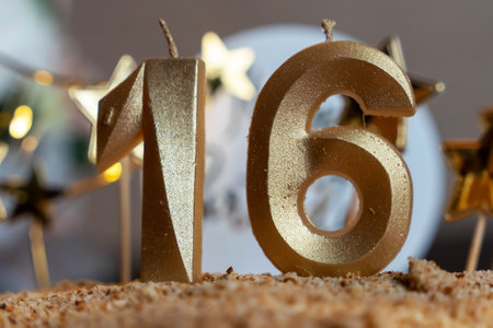 Golden sixteen birthday candles burning on cake with star decorationsの写真素材