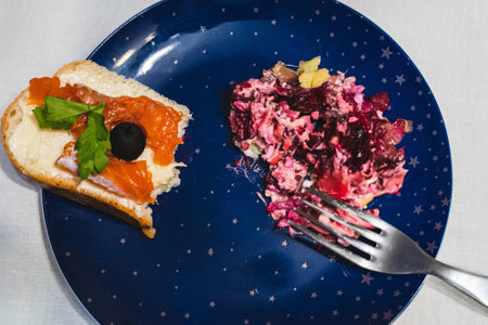 Partially eaten herring sandwich and beetroot salad with mayonnaise on a blue plate with golden starsの写真素材