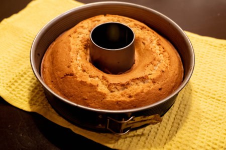 Freshly baked cake resting in its mold on a yellow kitchen towel, emitting a warm, inviting aromaの写真素材