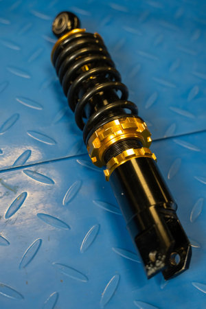 Close-up of a black and gold motorcycle shock absorber resting on a textured blue metal surfaceの写真素材