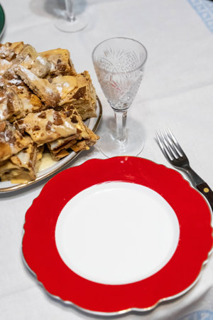 Red and white plate with golden rim waiting for napoleon cake dessert on white tablecloth next to crystal glass and forkの写真素材
