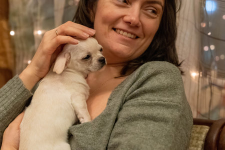 Woman cuddling a small white chihuahua puppy close to her chest, smiling and petting the dogの写真素材