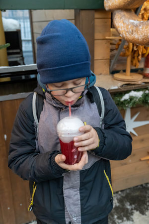 Schoolboy drinking hot cranberry juice at an outdoor christmas market, enjoying winter festivitiesの写真素材