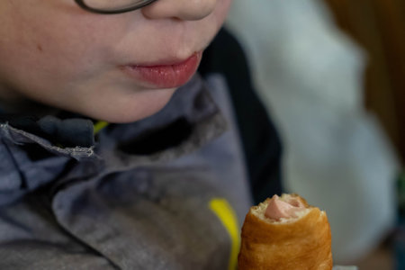 Close-up of child savoring a sausage roll, a popular savory pastry snackの写真素材