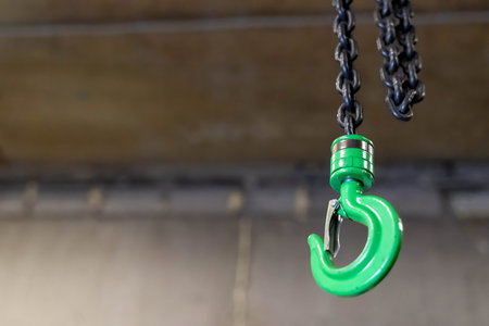 Green lifting hook hanging from chain, ready for industrial operations