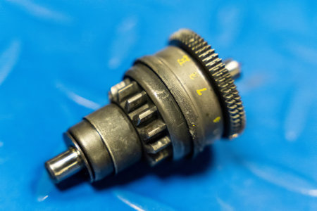 Close-up of a worn motorcycle starter gear resting on a blue backdrop, highlighting its metallic components and numbered settingsの写真素材