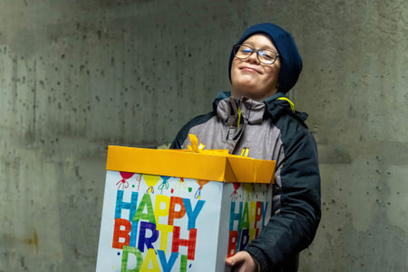 Boy wearing winter clothes holding a large colorful birthday gift box and smilingの写真素材