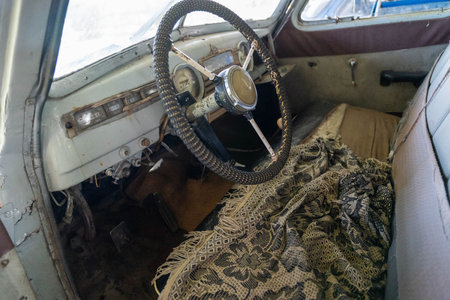 An old car's interior showcases a classic steering wheel and worn seats.の写真素材