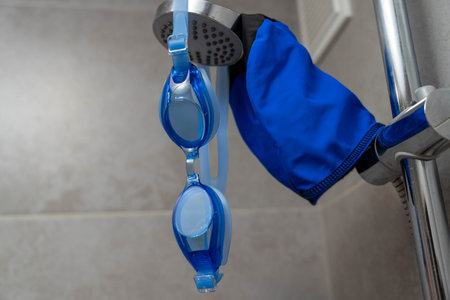 A pair of colorful swimming goggles and a matching cap hanging on a shower room hook, ready to be used for a refreshing swim at the pool or an invigorating session of water aerobics.の写真素材