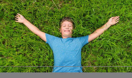 A person enjoying a peaceful moment while lying in lush green grass with arms outstretchedの写真素材