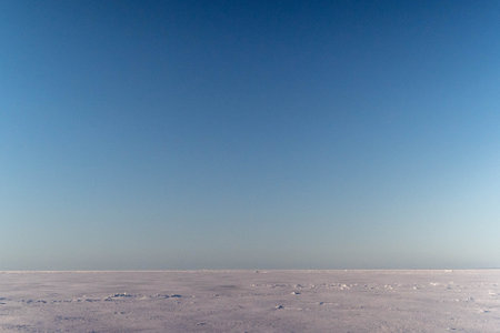 Frozen lake covered with snow under blue skyの写真素材