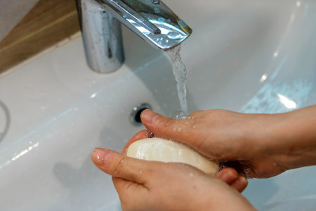 Woman washing hands with soap under running water in bathroom sinkの写真素材