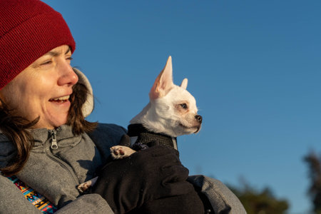 Woman wearing winter clothes holding small white chihuahua dog outdoorsの写真素材