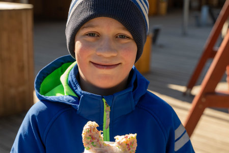 Smiling boy wearing beanie and blue jacket enjoying sweet treat outdoorsの写真素材