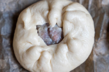 Raw baozi bun showing filling on baking paper: preparation in kitchenの写真素材