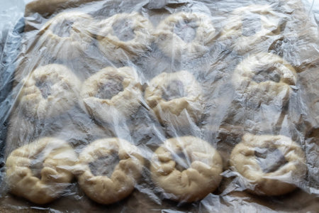 Raw buns covered with plastic wrap rising on baking sheetの写真素材