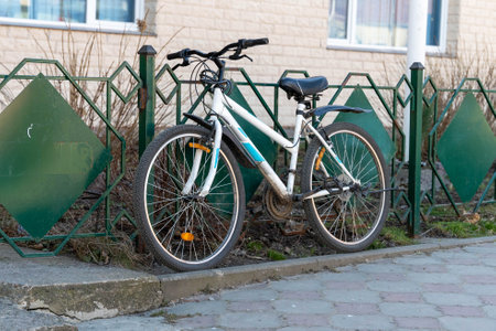 White and blue bicycle leaning against green metal fence in urban settingの写真素材
