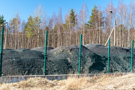 Large piles of coal behind a metal fence are polluting the environment near a forestの写真素材