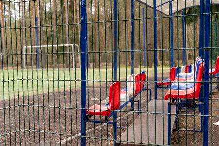 Empty red and white plastic chairs on sidelines of soccer field behind fenceの写真素材