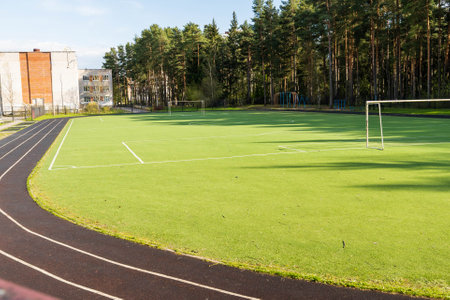 Empty football field with running track surrounded by trees on sunny dayの写真素材