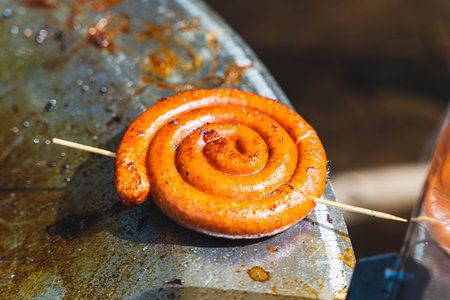 Grilled spiral sausage cooking on a hot surface with wooden skewerの写真素材