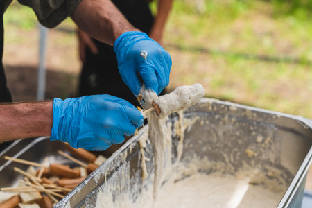 Chef dipping hot dogs in batter, preparing corn dogs at outdoor event