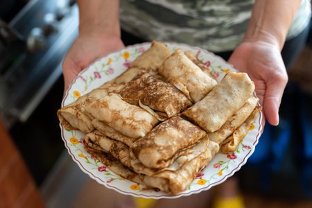 Hands holding plate of cooked pancakes blini crepes