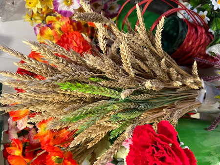 Dried wheat bouquet with vibrant red flowers and colorful floral arrangements in the background, showcasing natural beauty and decorative elements for home decorの写真素材