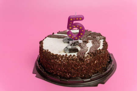 Chocolate cake with decorative frosting and a bright pink background, featuring a number five candle, perfect for birthday celebrations and festive occasionsの写真素材