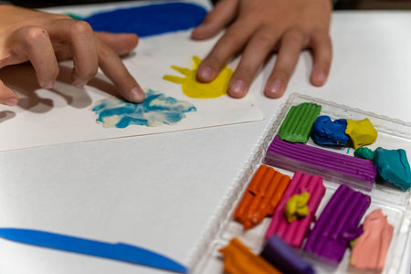 Childs hands creating colorful shapes with modeling clay on a white surface, showcasing creativity and artistic expression in a playful environment with vibrant materialsの写真素材