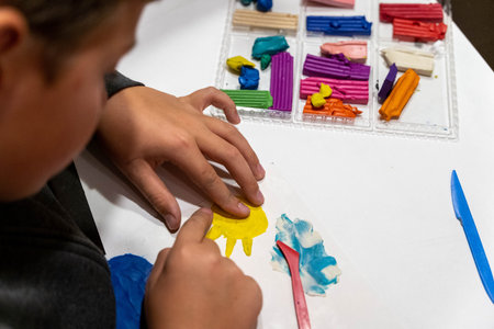 Child creating colorful clay art with hands, focused on shaping yellow figure, surrounded by various...