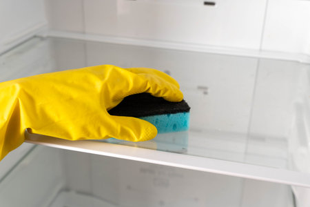 Cleaning a refrigerator shelf with a sponge in a kitchen during the dayの写真素材