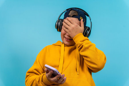 Child enjoys music on phone while wearing headphones against a blue backdrop