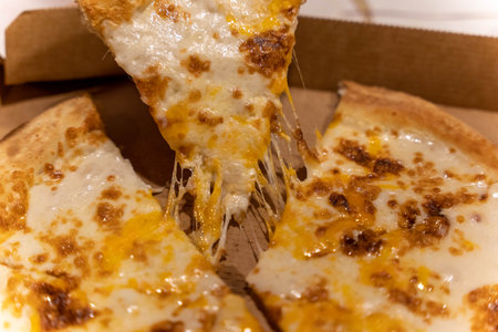 Cheese pizza with melted cheese pulled from the box at a gatheringの写真素材