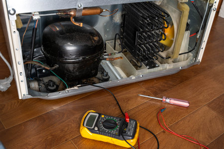 Appliance technician inspecting a refrigerator compressor and condenser coils with a multimeter and...