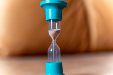 Hourglass with turquoise top and base is placed on a wooden surface, sand flowing through the glass...