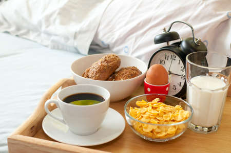 Breakfast in Bed - Rolls, Coffee, Boiled Egg, Milk, Corn Flakes and Alarm Clockの写真素材