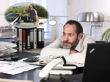 Mature businessman at desk with a thought bubble of himself and new car countryside. Horizontal shotの写真素材