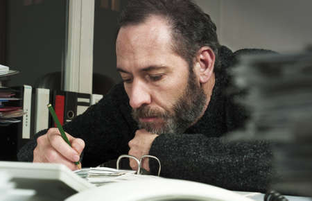 Mature businessman writing on papers at office-overworked at night time. Horizontal shotの写真素材
